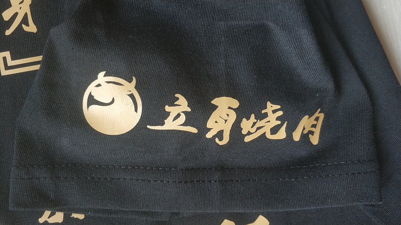 黑色餐饮工服下摆烫金牛头logo与书法字样特写